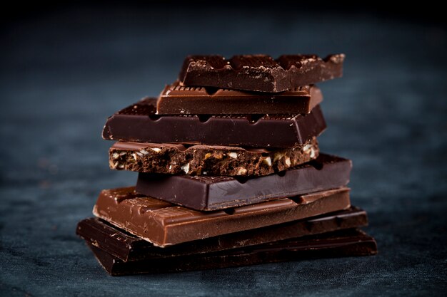 Chocolate bars pieces stack on black background.