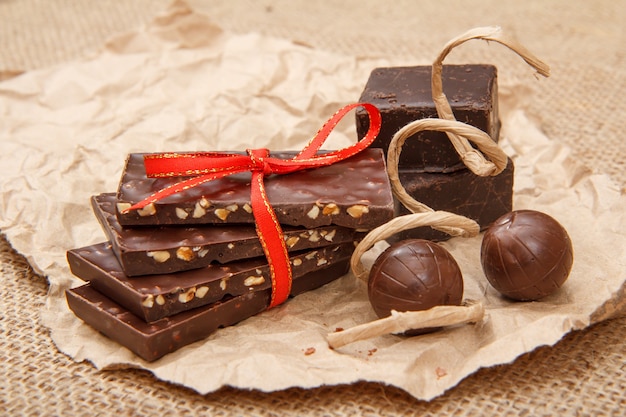 Плитки шоколада с орехами, перевязанные красной лентой, и шоколадные конфеты на листе упаковочной бумаги.