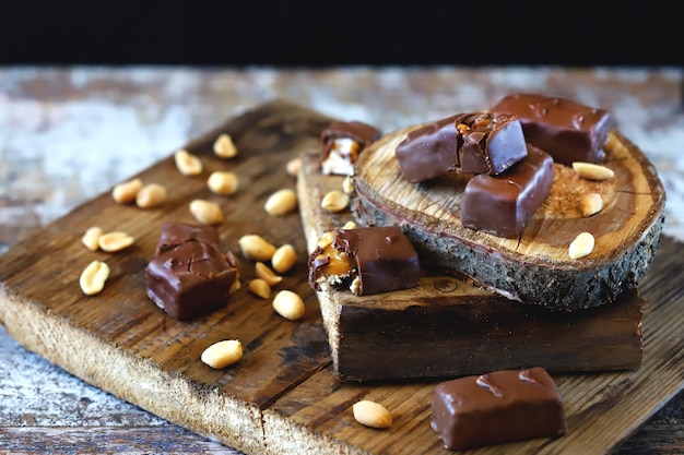 Chocolate bars with peanuts and caramel on wooden board.