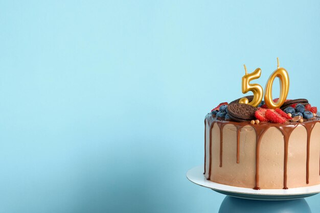 Photo chocolate birthday cake with berries cookies and number fifty golden candles on blue background