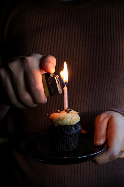 Photo chocolate birthday cupcake with a single candle light on dark background