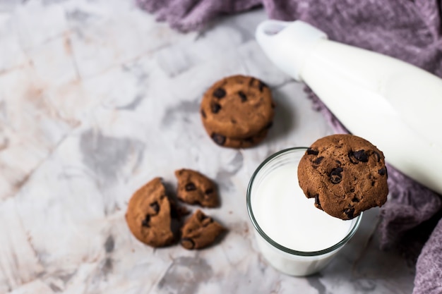 Chocolate biscuits next to a glass bottle and a glass of milk on a gray table