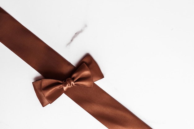 Chocolate brown silk ribbon on marble background flatlay