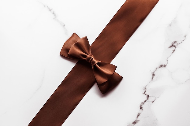 Chocolate brown silk ribbon on marble background flatlay