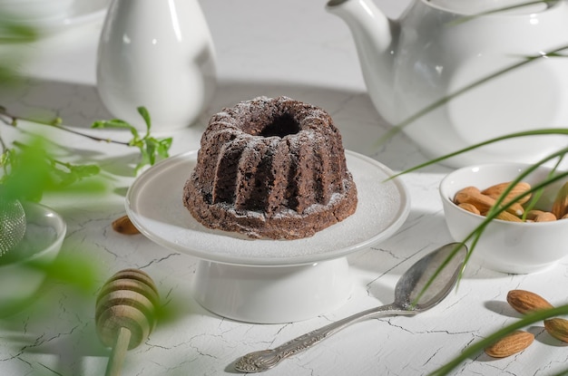 Chocolate brownie with almonds and powdered sugar on a white stand with hard light with selective focus