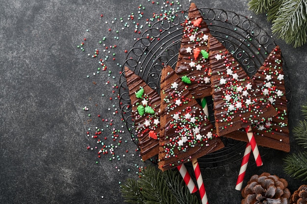 Chocolate brownies christmas tree with chocolate icing and\
festive sprinkles on stone table christmas food ideas sweet\
homemade christmas holidays pastry concept holiday cooking concept\
top view