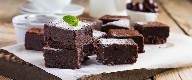 Chocolate brownies with powdered sugar and cherries on a dark wooden background. Selective focus.