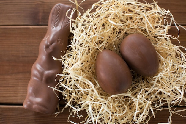 chocolate bunny and eggs in straw nest on wood