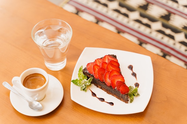 Chocolate cake, brownie with strawberries and mint, espresso, glass of water on a wooden table