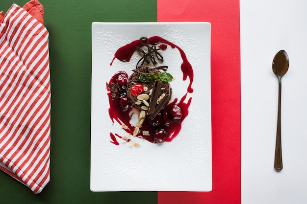 빨간색 녹색과 흰색의 대조적인 화려한 배경에 초콜릿 케이크 체리 아몬드와 민트 탑 뷰 사진으로 장식된 레스토랑에서 제공되는 맛있는 디저트