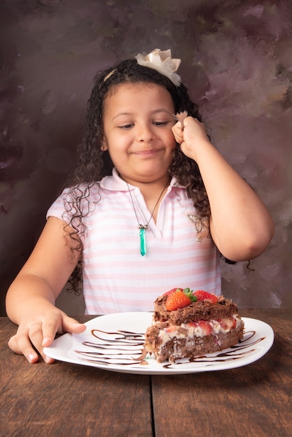 チョコレートケーキ、イチゴとチョコレートケーキの美しい部分を持つかわいい女の子、選択的な焦点。