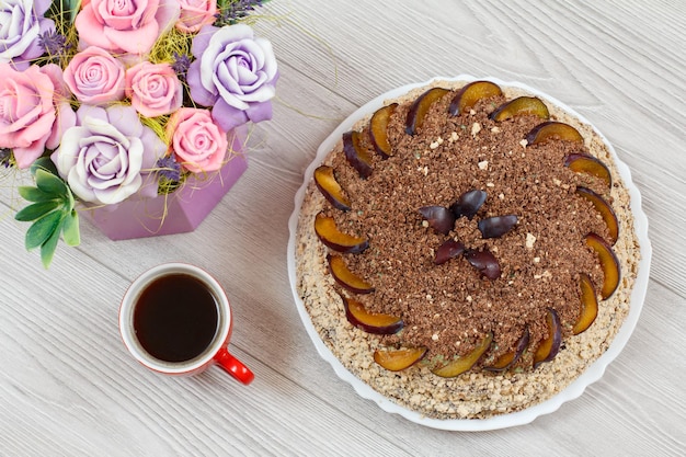 Torta al cioccolato decorata con prugne e tazza di caffè accanto su tavole di legno grigie.