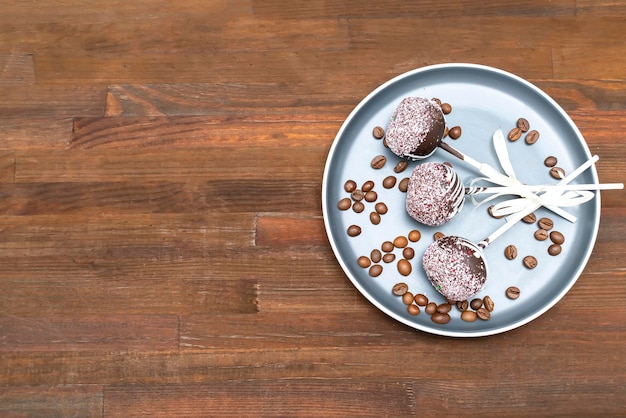 Chocolate cake pops decorated white sprinkles on plate with coffee beans on wooden background copy space, Delicious pastry, desserts on stick. Tasty food flat lay, lay out, top view.