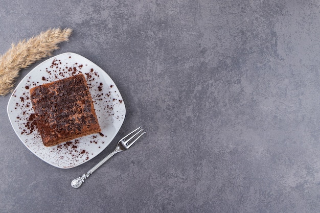 石のテーブルの上に置かれた白いプレートにカカオを粉末にしたチョコレートケーキ。