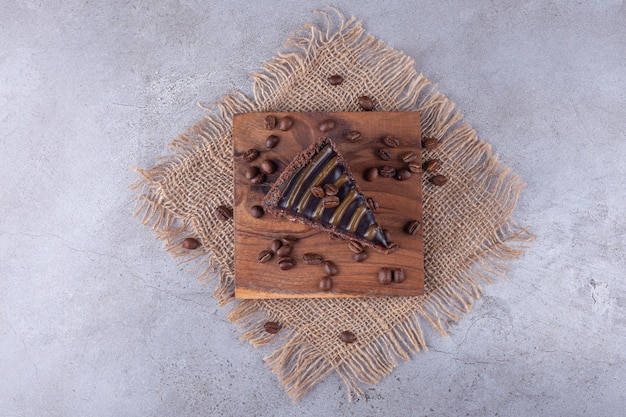 Chocolate cake slice with coffee beans placed on sackcloth surface .