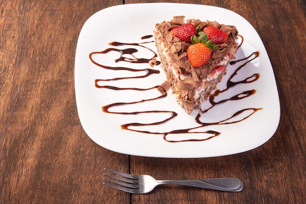 Chocolate cake, a tasty slice of chocolate cake with strawberries on a white plate on rustic wood, abstract background, selective focus.