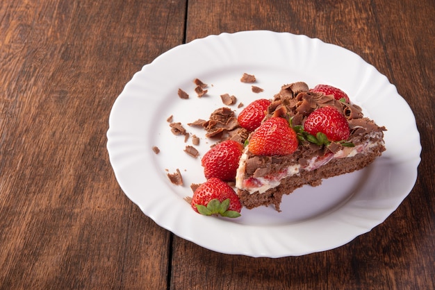 Chocolate cake, a tasty slice of chocolate cake with strawberries on a white plate on rustic wood, abstract background, selective focus.