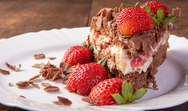 Chocolate cake, a tasty slice of chocolate cake with strawberries on a white plate on rustic wood, abstract background, selective focus.