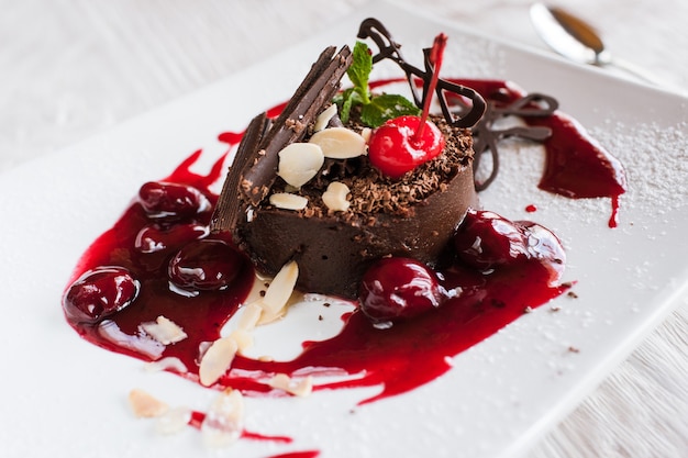 Chocolate cake on white plate with decoration from cherry, almond and mint.