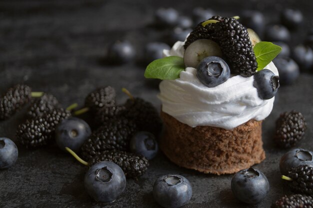 Chocolate cake with berries, blueberry and mulberry. On a black background. A dark photo.