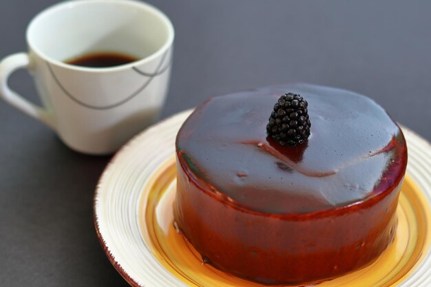 A chocolate cake with a blackberry on top, and a cup of coffee.