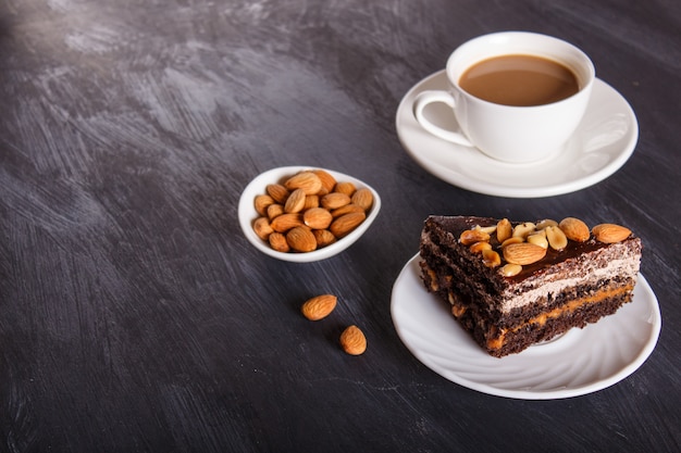 Chocolate cake with caramel, peanuts and almonds on a black wooden background. 