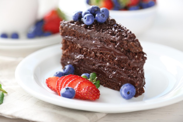 Chocolate cake with chocolate cream and fresh berries on plate on light background