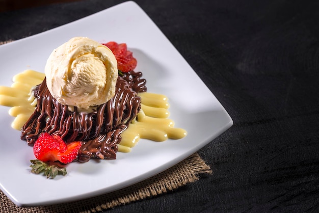 Chocolate cake with  chocolate icing ice cream and slice of strawberry on black wood