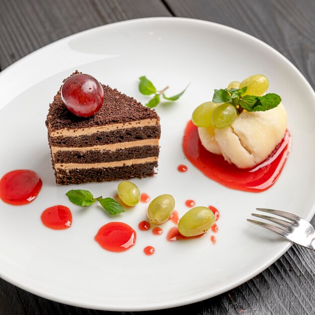 Chocolate cake with ice cream and grapes on a white plate