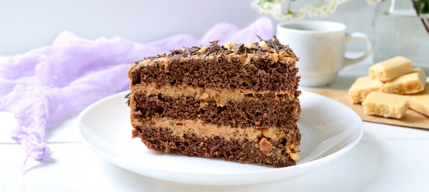 Chocolate cake with nut cream on a white wooden table. A piece of cake on a plate and a cup of coffee.