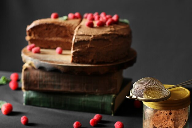 Фото Шоколадный торт с малиной на книгах. торт на темном фоне. сито и какао