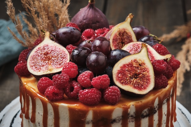 Chocolate cake with raspberry filling, garnished with fresh figs, grapes and raspberries. Rustic cake on a wooden table.
