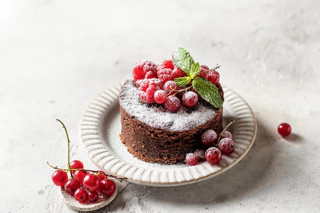 Chocolate cake with red berries mint leaves and snowy powdered\
sugar close up on white textured