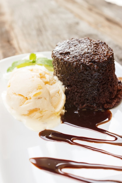 Chocolate cake with rum raisin ice cream and whipping cream on white plate.