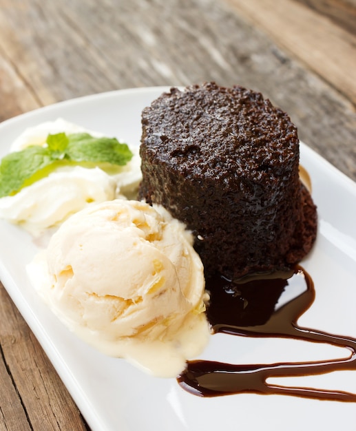 Torta al cioccolato con gelato all'uvetta di rum e panna da montare sul piatto bianco.