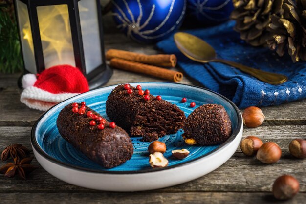 사진 초콜릿 케이크 크리스마스 장식으로 견과류와 고추를 곁들인 감자 크리스마스 장식이 있는 어두운 나무 배경의 파란색 접시에 초콜릿 케이크