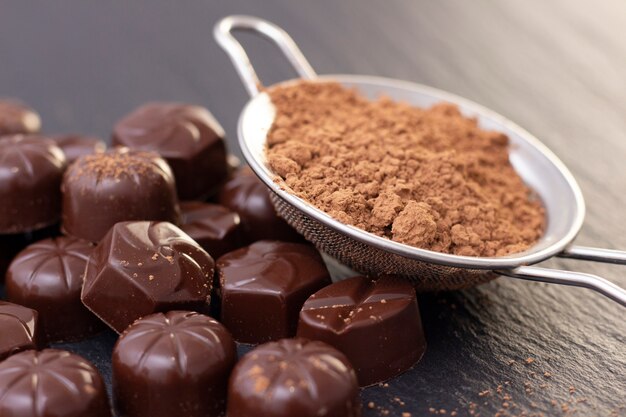 Chocolate candies on a black surface, cocoa powder. dark photo, mood.