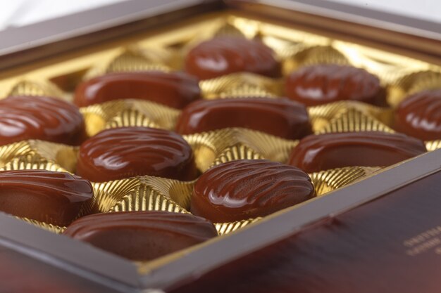 Chocolate candies in box, close up view on white table