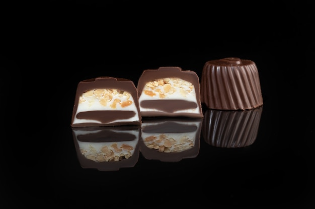 Chocolate candies on a dark surface with reflection. Filling of nuts and fruits. Copy space.