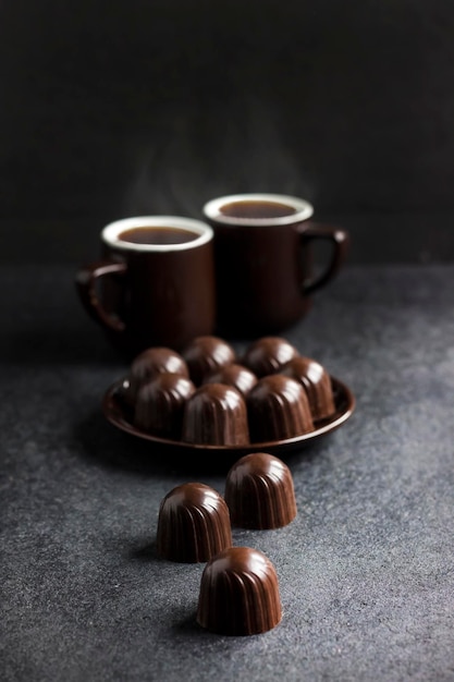 Chocolate candies on a plate and two cups of coffee on black background