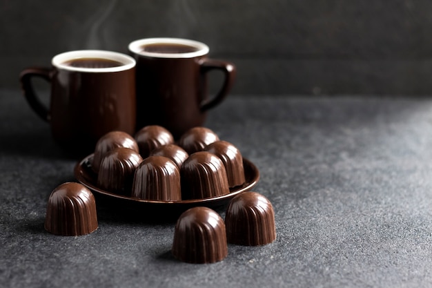 Chocolate candies on a plate and two cups of coffee on black surface