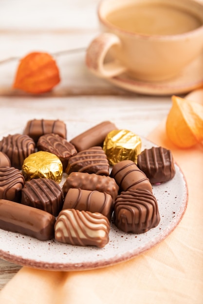 Caramelle al cioccolato con tazza di caffè e fiori di physalis su un fuoco selettivo di vista laterale del fondo di legno bianco