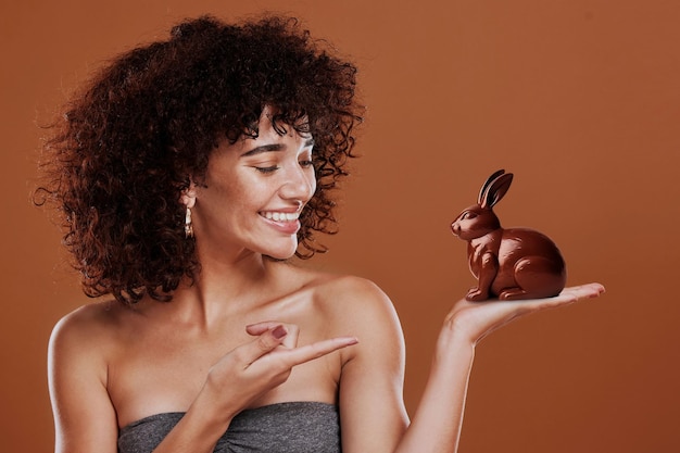 Chocolate candy and bunny with woman and pointing in studio for easter sweets or sugar cocoa food an