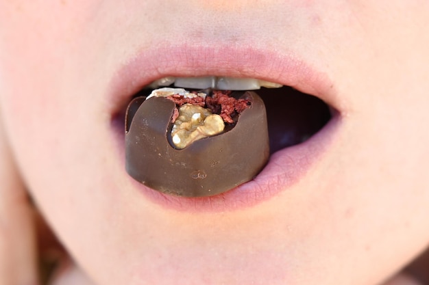 A chocolate candy in the mouth close up woman eating chocolate\
holding candy in mouth