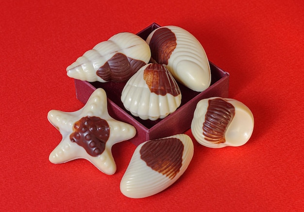 Foto conchiglie di caramelle al cioccolato su sfondo rosso