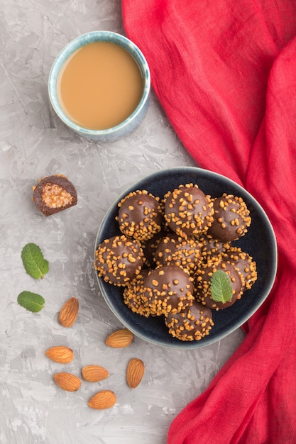 Chocolate caramel ball candies with almonds and a cup of coffee on a gray concrete surface and red textile