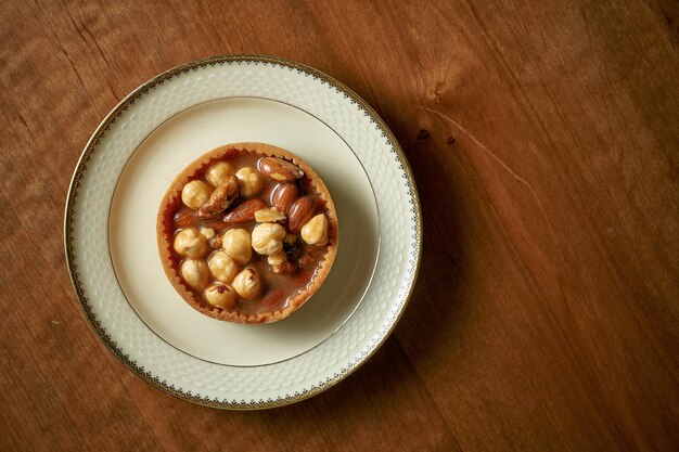 Chocolate caramel tart with nuts in a white plate on a wooden background