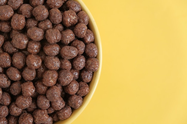 Chocolate cereal corn balls in a yellow bowl on a yellow background