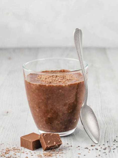 Chocolate chia pudding in glass and chocolate cubes slice on gray wooden table.