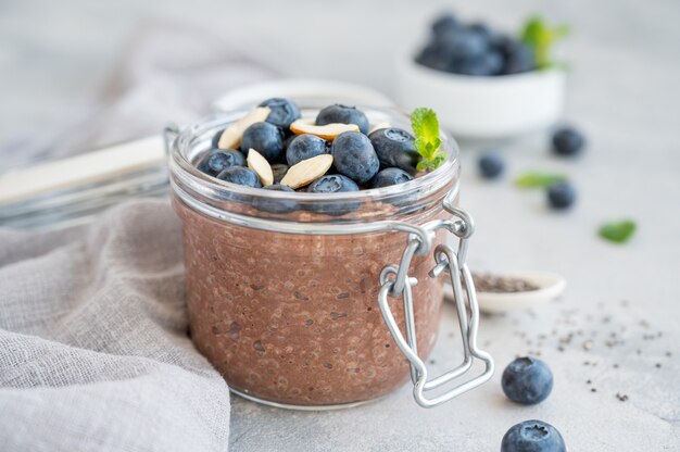 Chocolate chia pudding with blueberry, almonds and mint on top in a glass jar on a gray concrete background. Healthy food. Copy space.
